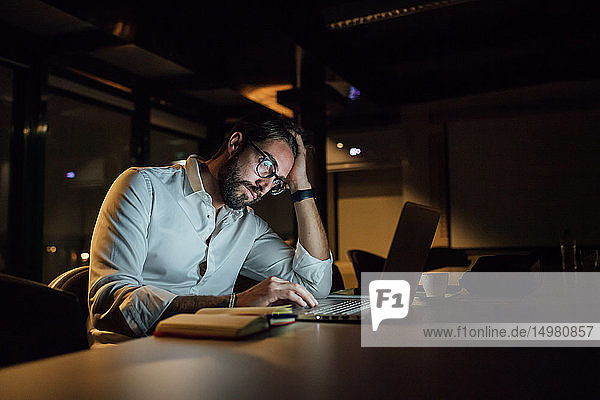 Müde Geschäftsmann nachts im Büro beim Tippen am Laptop