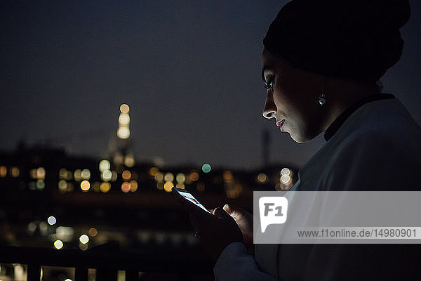 Junge Geschäftsfrau sieht nachts auf dem Balkon des Büros nach einem Smartphone