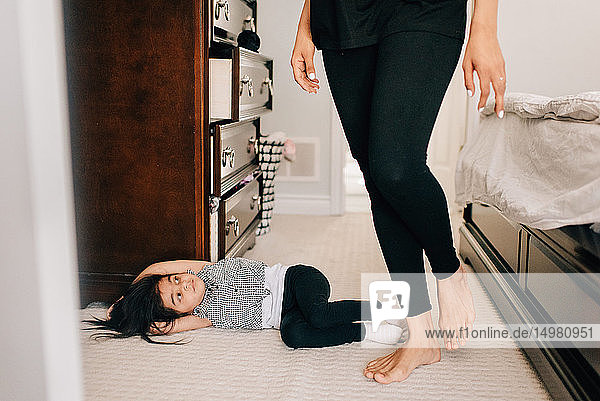 Girl lying on bedroom floor looking up at mother