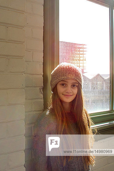 Teenage girl with long brown hair and knit hat by window  portrait