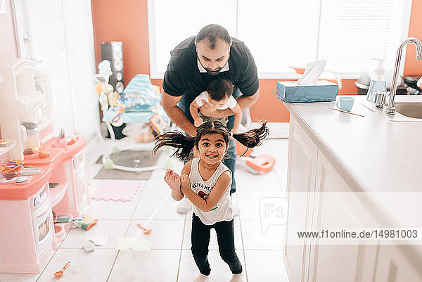 Girl playing in kitchen in front of father and baby brother  portrait