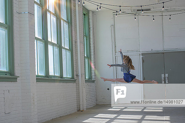 Teenager-Mädchen mit langen braunen Haaren springt im Tanzstudio in die Luft