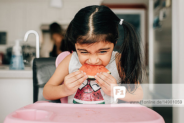 Mädchen im Hochstuhl isst Wassermelone