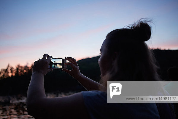 Frau fotografiert Sonnenuntergang mit Smartphone