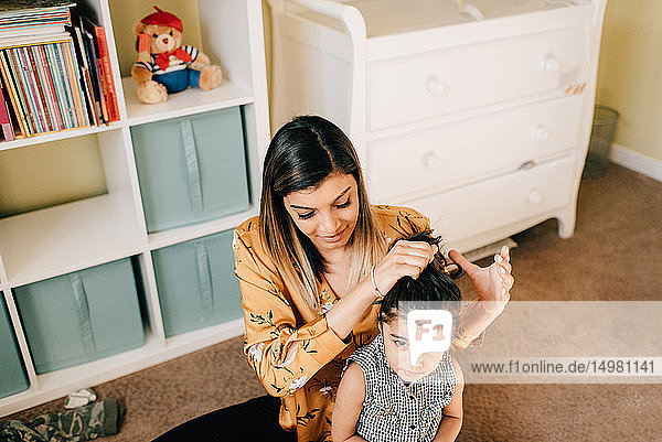 Mädchen sitzt auf dem Kinderzimmerboden  während die Mutter ihr Haar frisiert
