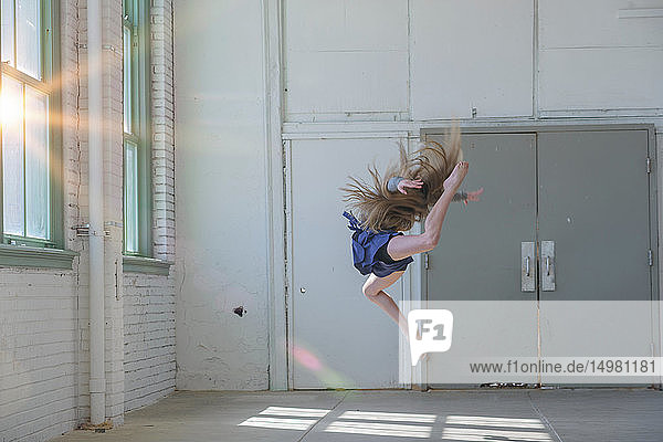 Teenager-Mädchen mit langen braunen Haaren springt im Tanzstudio in die Luft
