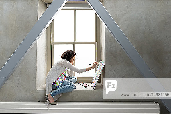 Junge Malerin malt Leinwand auf Atelier-Fensterbrett