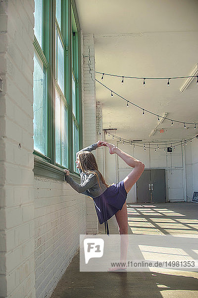Teenager-Mädchen blickt durch ein Tanzstudio-Fenster und hält ein erhobenes Bein