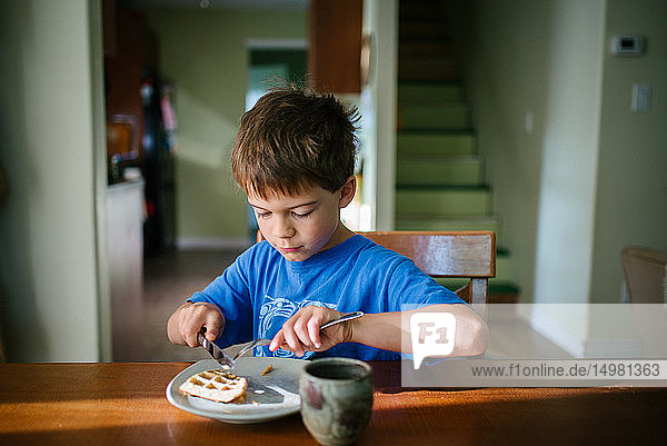 Junge isst Waffelfrühstück am Küchentisch