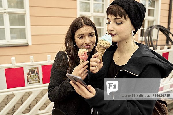 Two women with ice cream cones in hands using smartphone  in city Cottbus  Brandenburg  Germany.