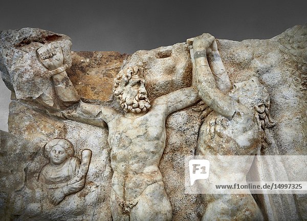 Close up of a Roman Sebasteion relief sculpture of Zeus and Prometheus  Aphrodisias Museum  Aphrodisias  Turkey. Against a grey background.Prometheus is screaming in pain. Zeus had given him a terrible punishment for giving fire to man: he was tied to the Caucasus mountains and had his liver picked out daily by an eagle. Herakles shot the eagle and is undoing the first manacle. He wears his trade mark lion-skin and thrown his club to one side. A small mountain nymph  holding a throwing stick appears amongst the rocks.