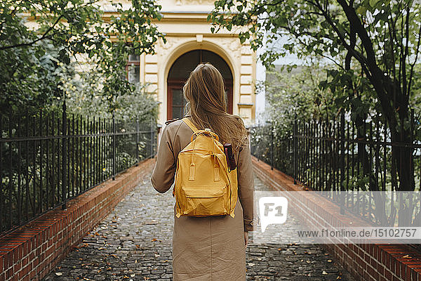 Junge Frau mit gelbem Rucksack geht im Park spazieren