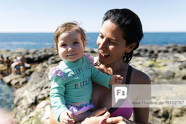 Frau hält ihre kleine Tochter auf Felsen am Strand