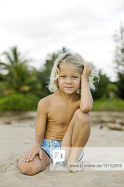 Blond haired boy kneeling on beach