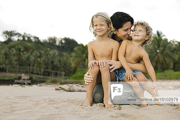 Frau mit ihren Söhnen auf dem Schoß am Strand sitzend