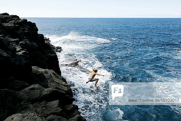 Junge springt von Klippe am Meer