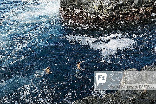 Father and son swimming in sea by cliffs