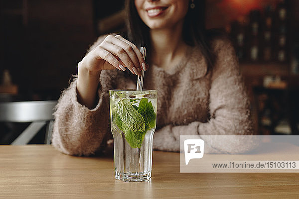 Woman holding straw in cocktail with mint leaves