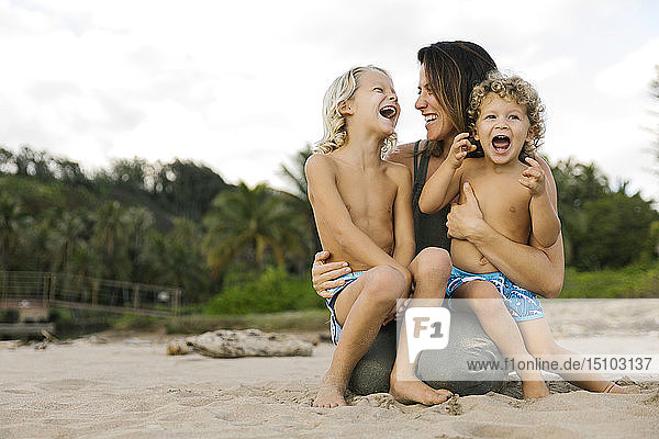 Frau mit ihren Söhnen auf dem Schoß am Strand sitzend