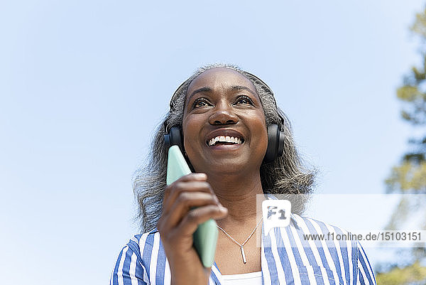 Lächelnde reife Frau beim Spaziergang mit Kopfhörern und Smartphone