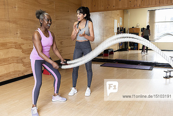 Personal Trainer ermutigt reife Frau  die mit Seilen im Fitnessstudio trainiert