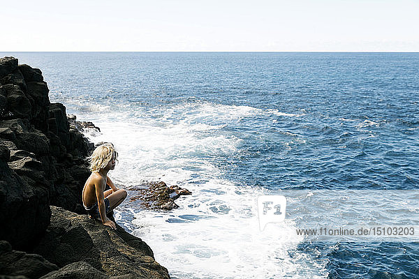 Junge hockt auf einer Klippe am Meer