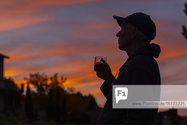 Silhouette eines Mannes mit Kaffeetasse bei Sonnenuntergang