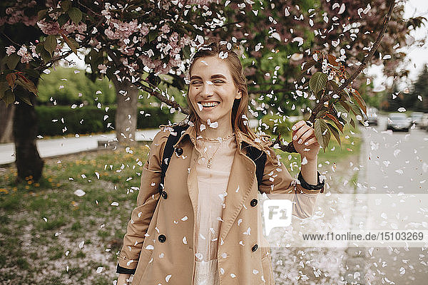 Lächelnde Frau zwischen fallenden Blütenblättern eines blühenden Baumes