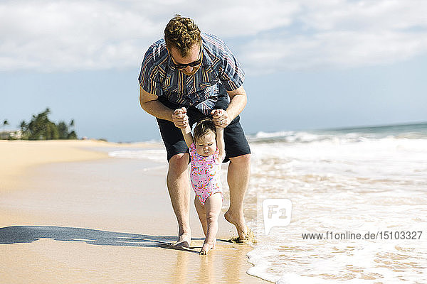 Father helping his baby girl walk on beach