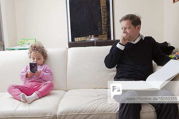 Mädchen benutzt Smartphone  während ihr Vater ein Buch liest