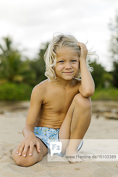 Blondhaariger Junge kniend am Strand