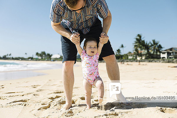 Vater hilft seinem kleinen Mädchen beim Laufen am Strand