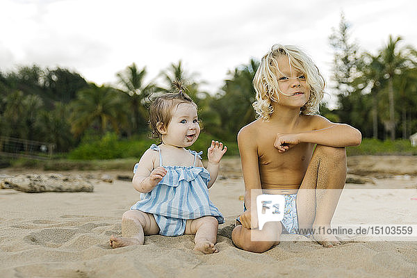 Junge und seine kleine Schwester sitzen am Strand