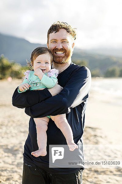 Man holding baby daughter on beach
