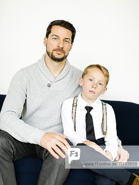 Well-dressed father and son sitting on sofa