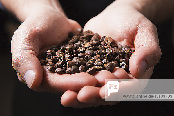 Geröstete Kaffeebohnen in den schalenförmigen Händen eines Mannes