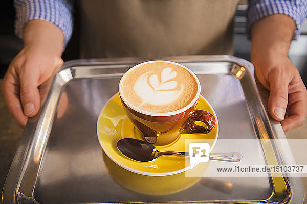 Barista hält eine gelbe Tasse Kaffee auf einem Tablett