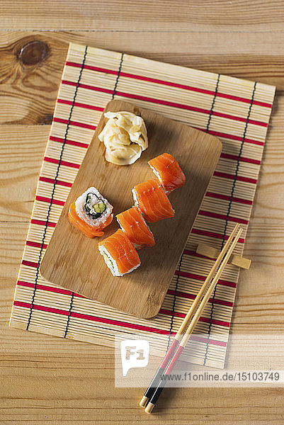 Lachs-Sushi auf Schneidebrett mit Stäbchen und Matte