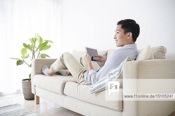 Young Japanese man using tablet on the sofa