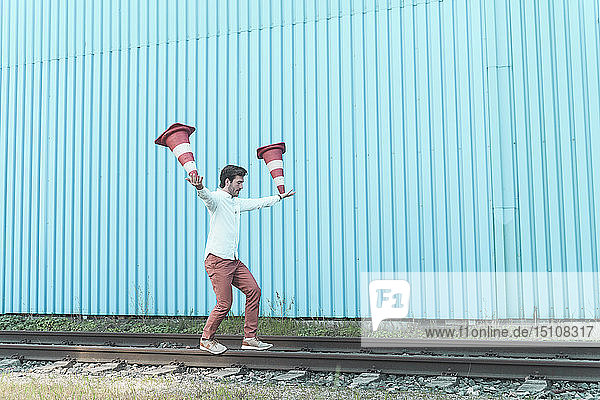 Junger Mann balanciert auf Schienen und jongliert mit Verkehrskegeln