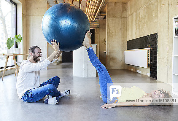Glücklicher Mann und Frau üben mit dem Fitnessball im modernen Büro