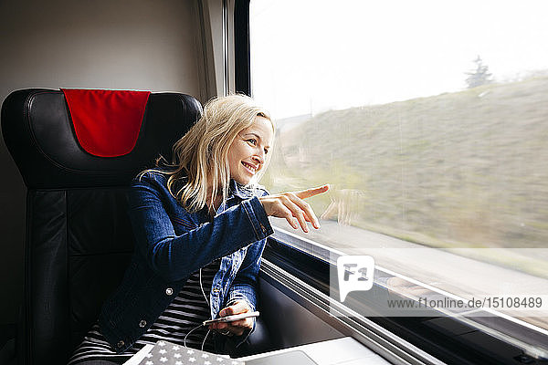 Lächelnde blonde Frau  die mit dem Zug reist und aus dem Fenster schaut