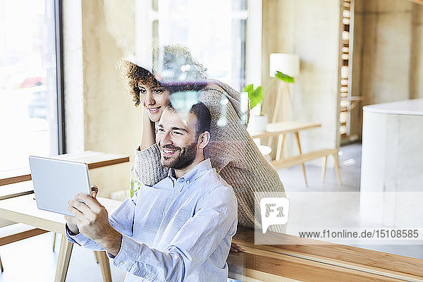 Lächelnder Mann und lächelnde Frau teilen sich ein Tablet in einem modernen Büro