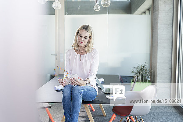 Businesswoman sitting on desk in office using cell phone