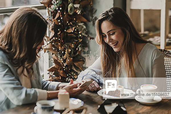 Zwei glückliche junge Frauen mit Handy-Treffen in einem Café