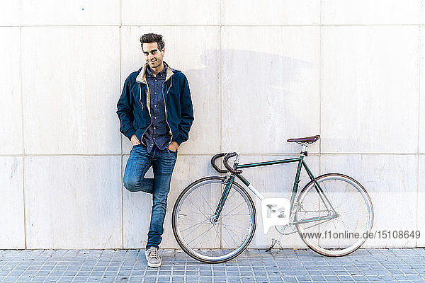 Portrait of casual man with bicycle standing at a wall