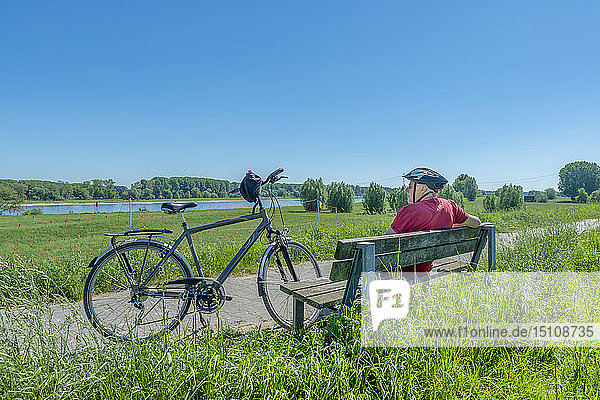 Germany  Zons  senior man with bicycle resting on a bench looking at view