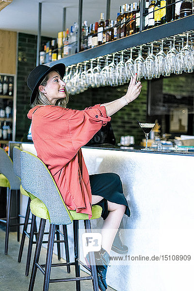 Happy woman sitting at the counter of a bar taking a selfie