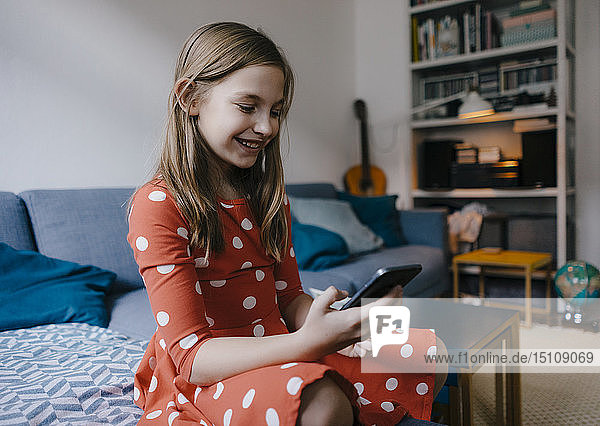 Glückliches Mädchen sitzt zu Hause auf der Couch und telefoniert mit dem Handy