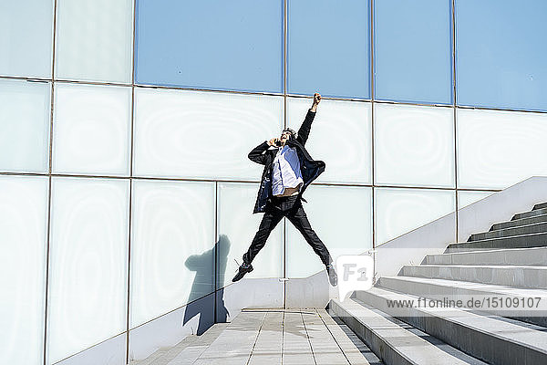 Excited businessman on cell phone jumping in the city